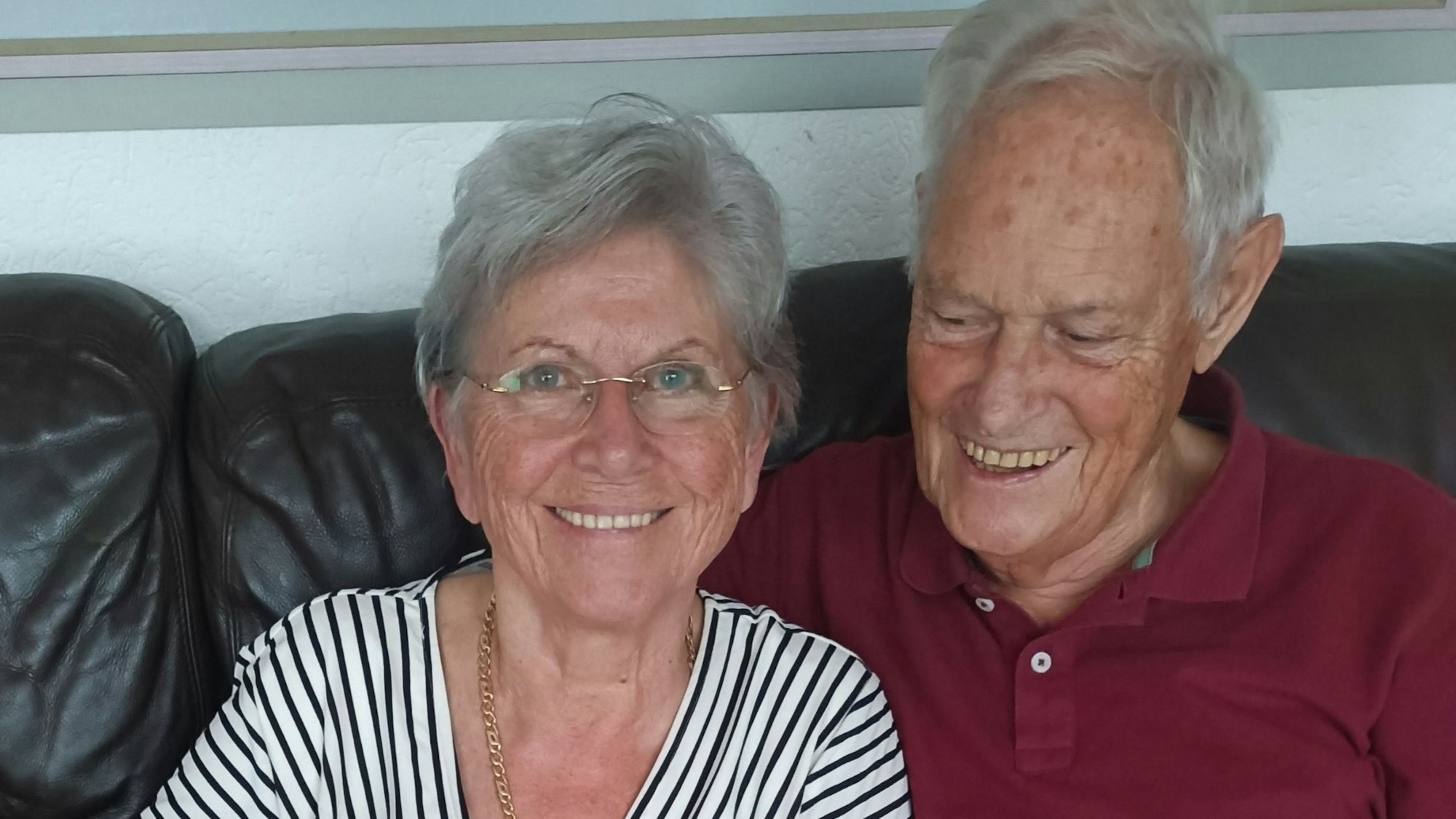Das Foto zeigt das Ehepaar, wie es auf einem schwarzen Sofa sitzt. Ingeborg lacht in die Kamera und Peter blickt lächelnd nach unten.