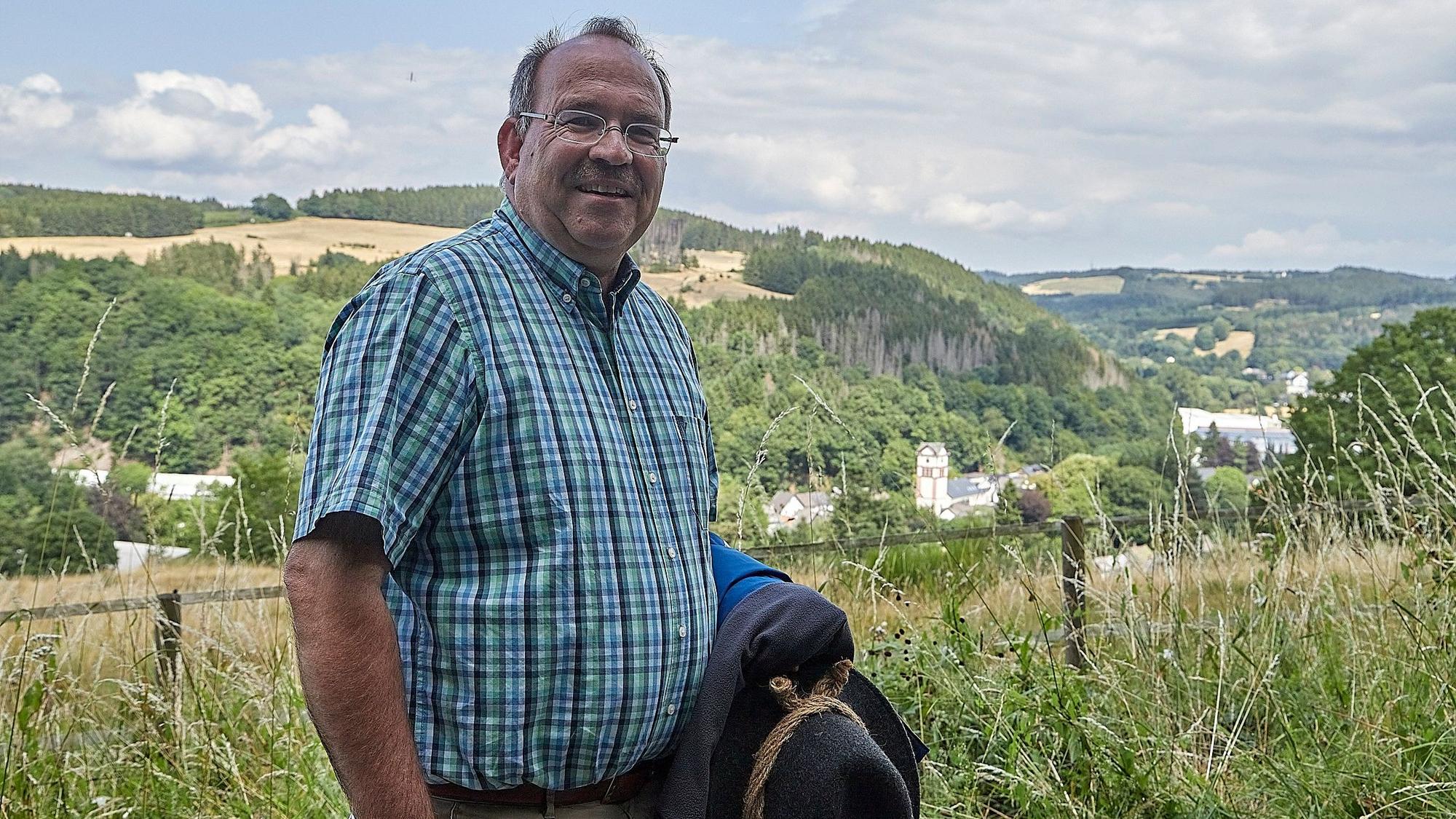 Ein Mann im rustikalen Wanderoutfit steht vor einer sommerlichen Eifellandschaft.