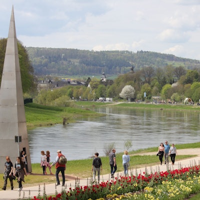 Am Ufer eines Flusses spazieren Menschen.