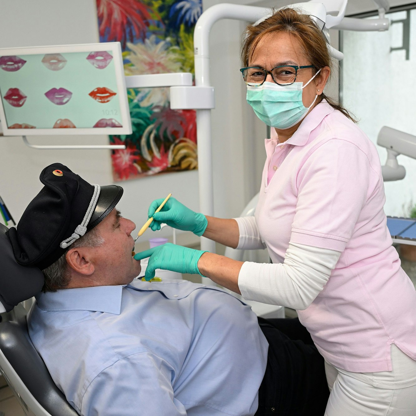 Eine Zahnärztin kontrolliert mit eine Zahnspiegel die Zähne im Mund eines Patienten.