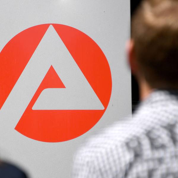 Zwei Personen stehen vor dem Logo der Agentur für Arbeit.