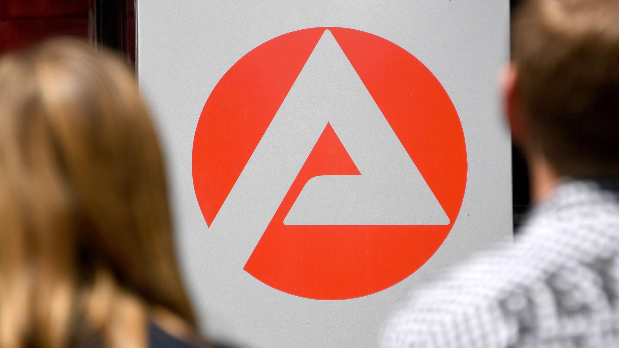 Zwei Personen stehen vor dem Logo der Agentur für Arbeit.