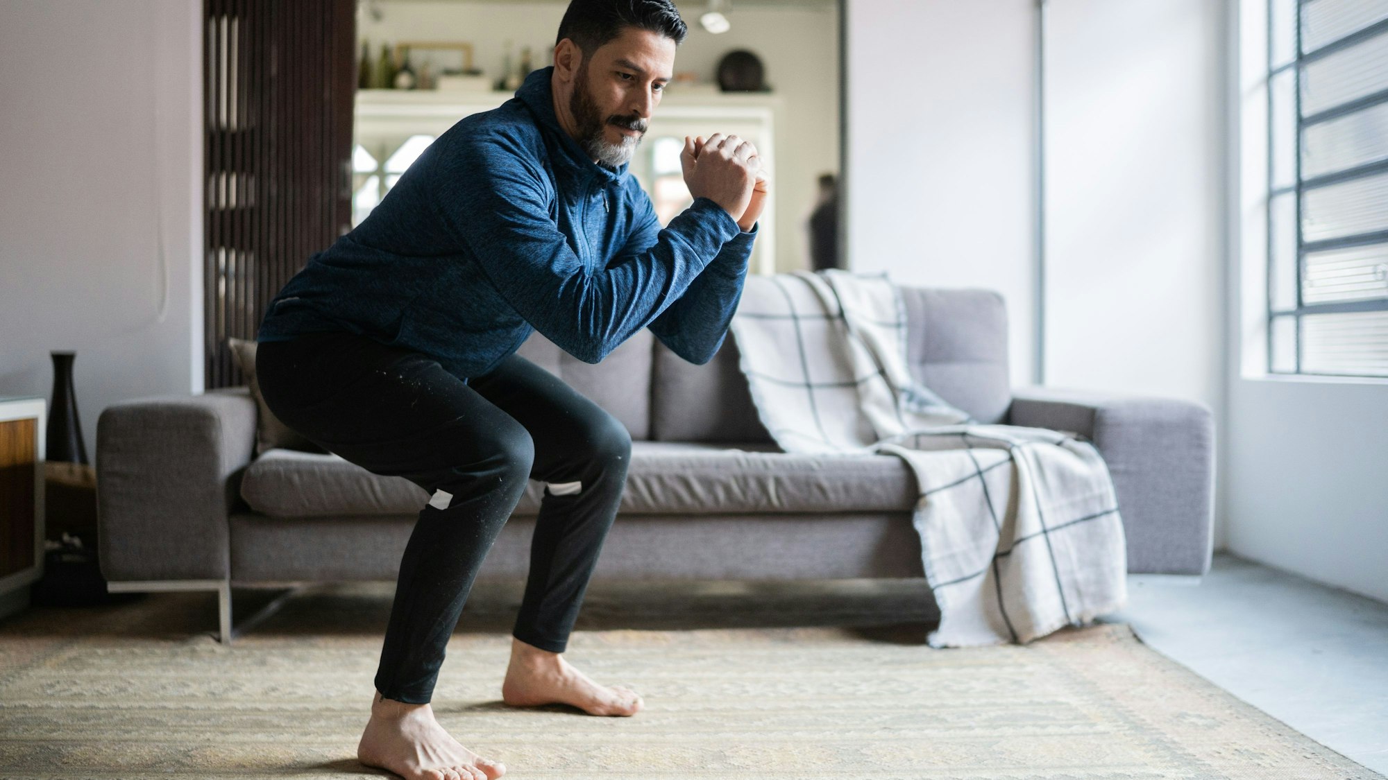 Ein älterer Mann führt zu Hause eine sogenannte Skihocke durch.