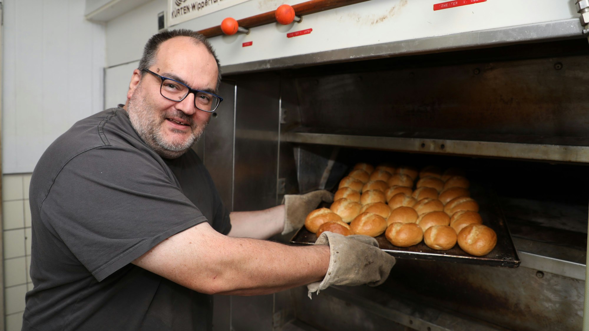 Bäckermeister Mario Fritzen zieht in der Backstube seiner Kürtener Bäckerei ein Blech mit Brötchen aus dem Ofen.