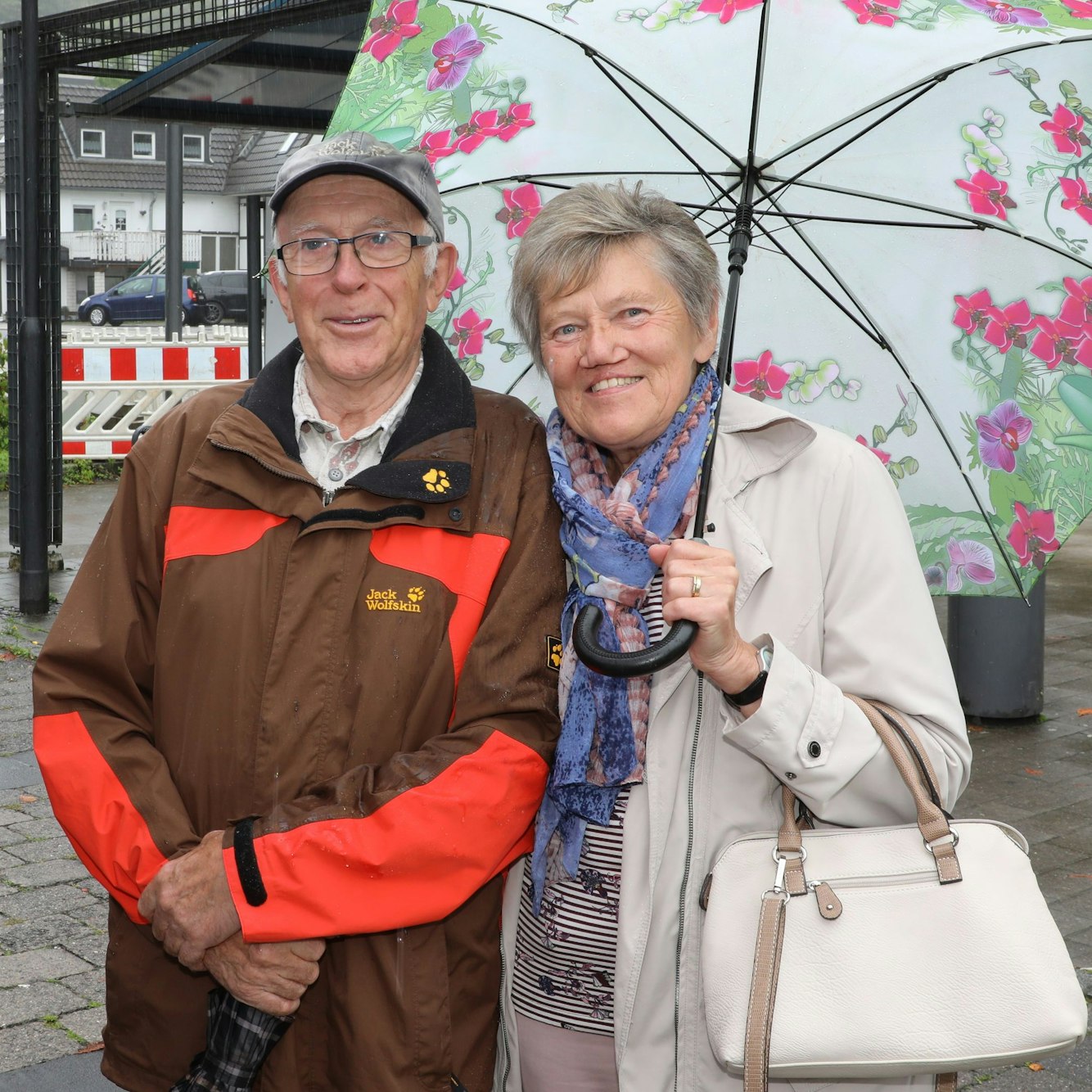 Zwei Menschen unter einem Schirm schauen in die Kamera.