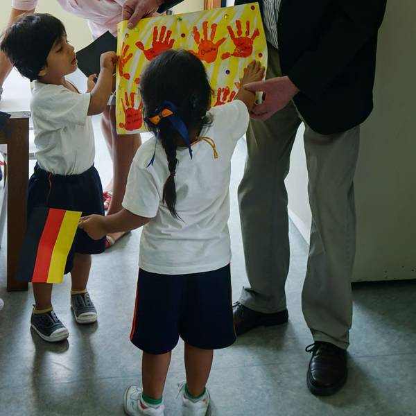 Manfred Görgens betrachtet ein Bild mit gelbem Hintergrund und roten Handabdrücken, das ihm Kinder zeigen.