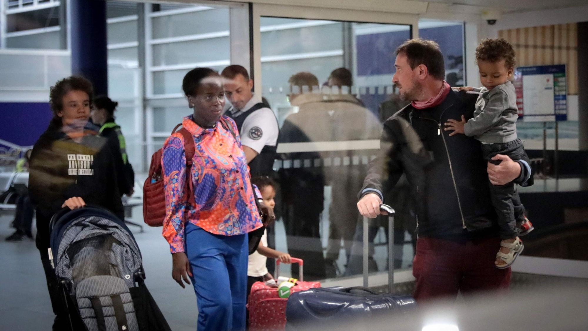 Erwachsene und Kinder stehen mit Gepäckstücken und einem Kinderwagen an einem Flughafen.