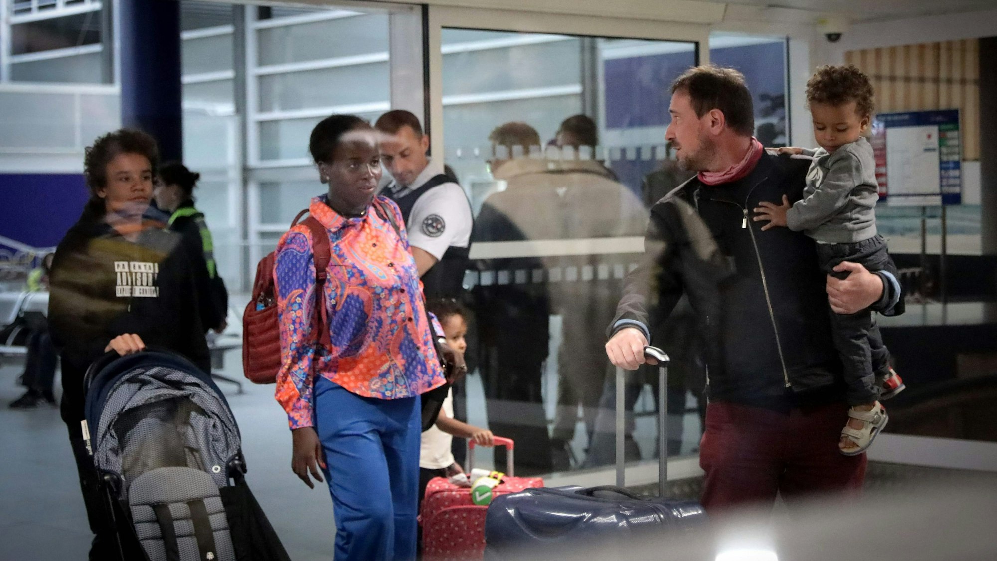 Erwachsene und Kinder stehen mit Gepäckstücken und einem Kinderwagen an einem Flughafen.