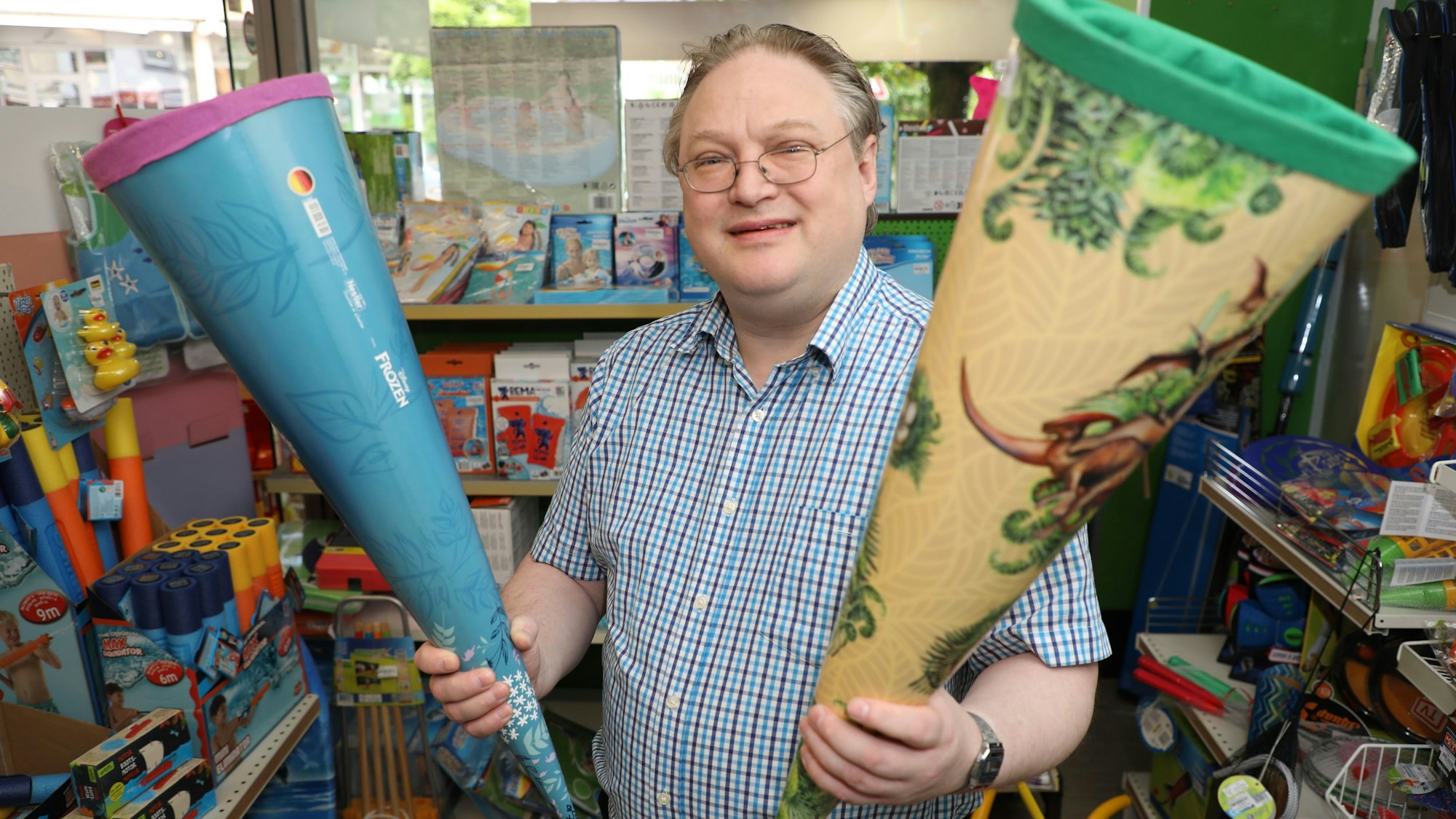 Der Inhaber von „Spiel & Spaß Daubenbüchel“ in Bensberg, Stefan Gutt, steht mit zwei Schultüten in den Händen vor einem Spielzeugregal.