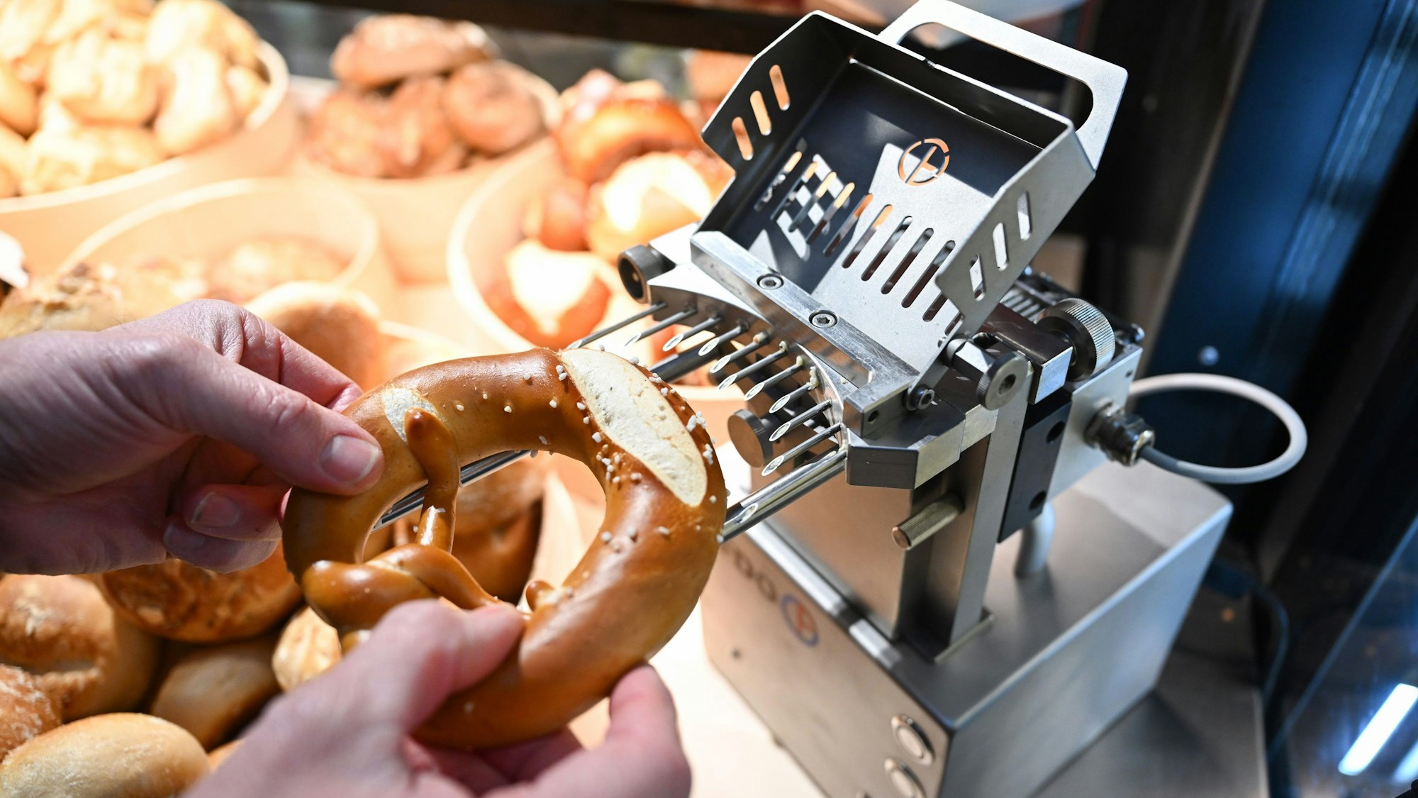 PRODUKTION - 02.02.2023, Baden-Württemberg, Stuttgart: In einem Bäckerei-Laden in der Markthalle befüllt ein Angestellter eine Brezel mit einer Brezel-Befüllungsmaschine mit Butter.
