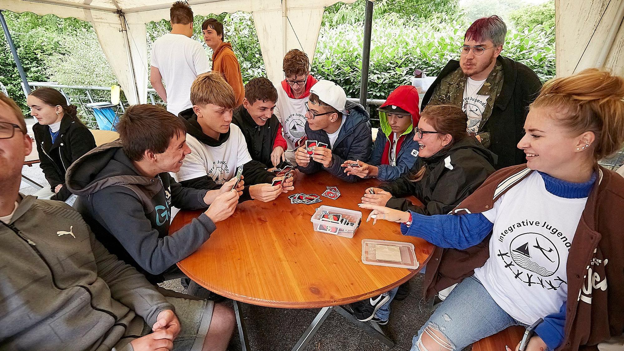 Um einen runden Tisch sitzen viele jugendliche Teilnehmer des Segelcamps und spielen das Kartenspiel Uno.
