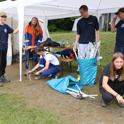 Mehrere junge Menschen bauen auf einem Zeltplatz einen Pavillon auf.
