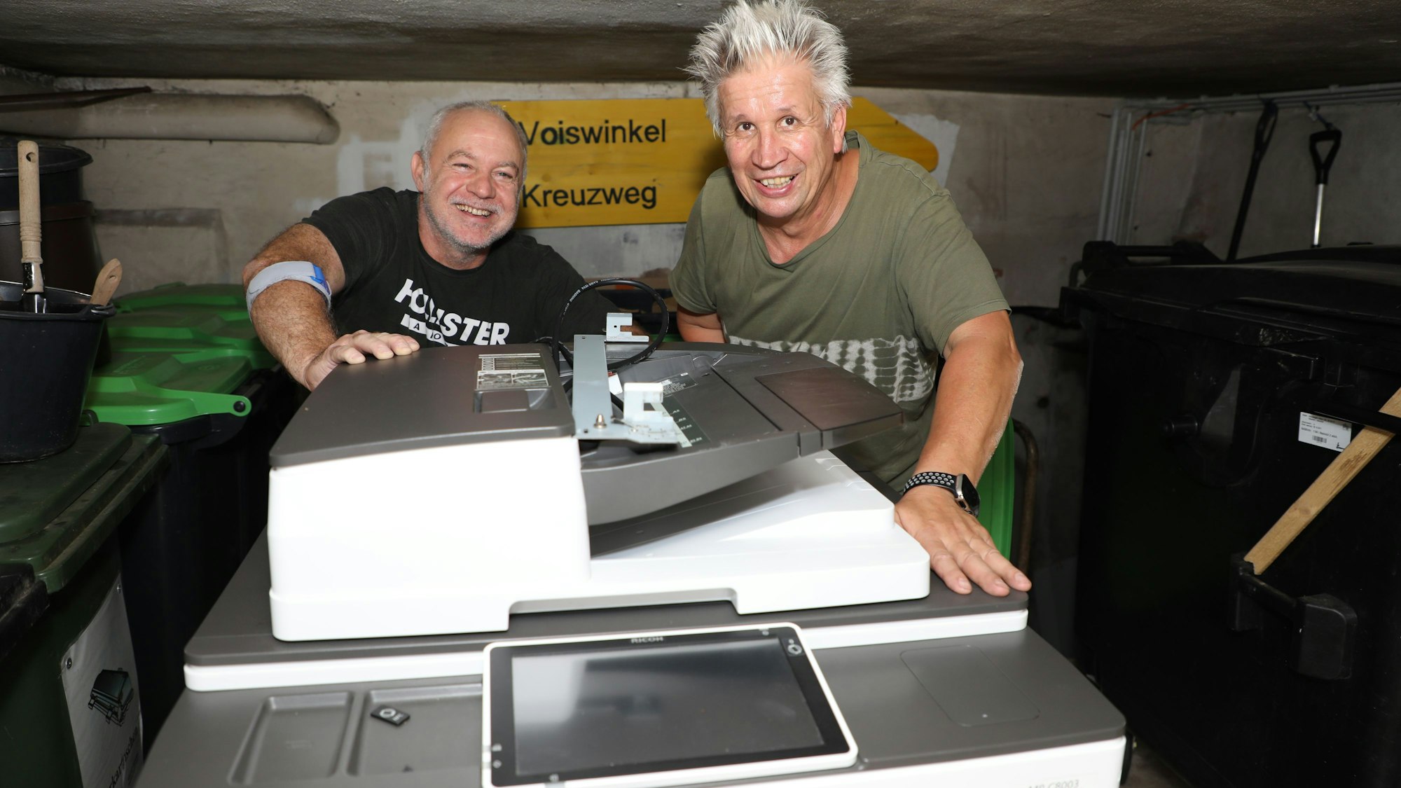 Zwei Männer schieben ein Kopiergerät durch einen niedrigen Keller im Rathaus Odenthal.