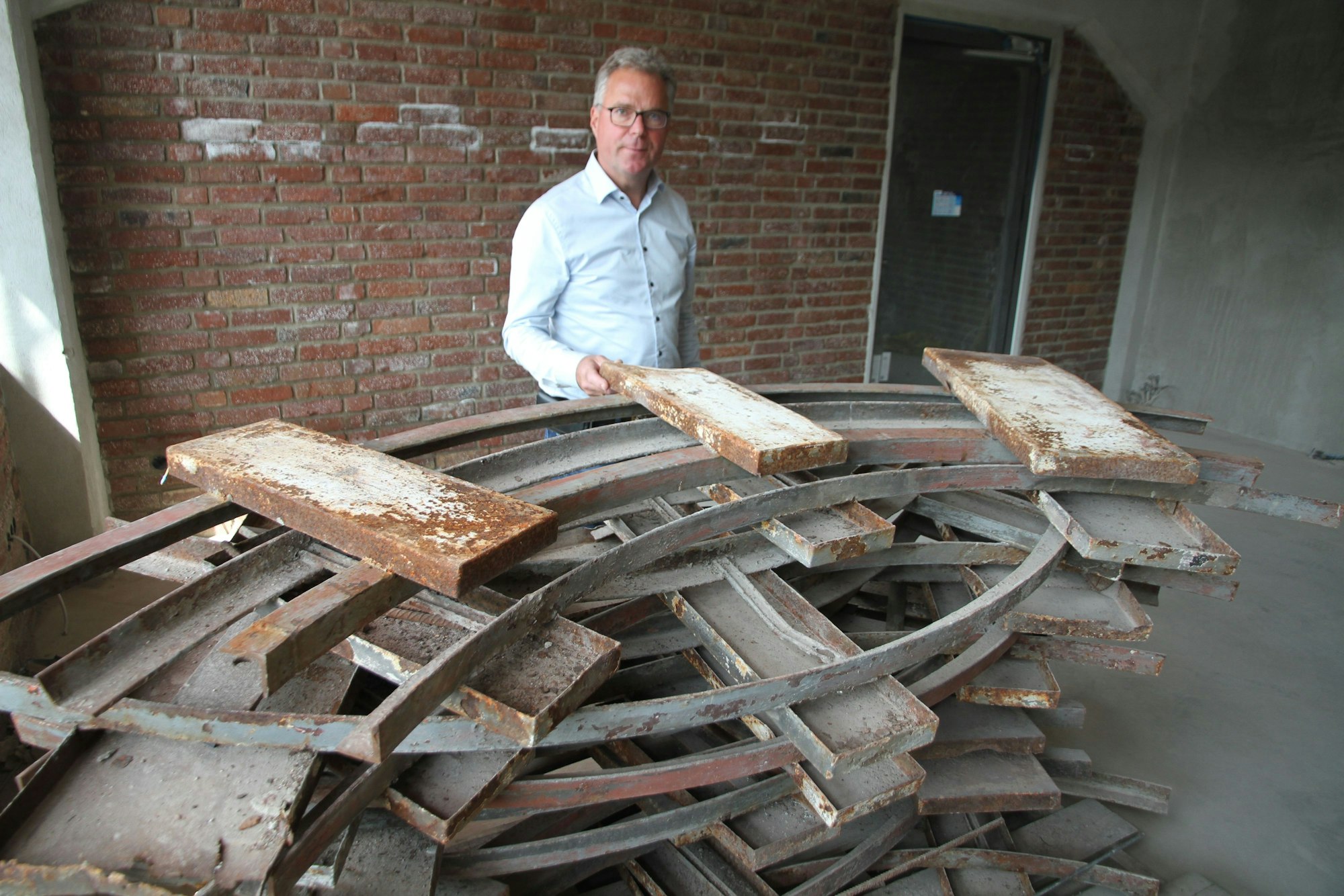 Ein Mann, der Siegburger Unternehmer Hannspaul Egge, steht hinter einer Palette mit den Resten der alten Turmuhren vom Phrixgelände