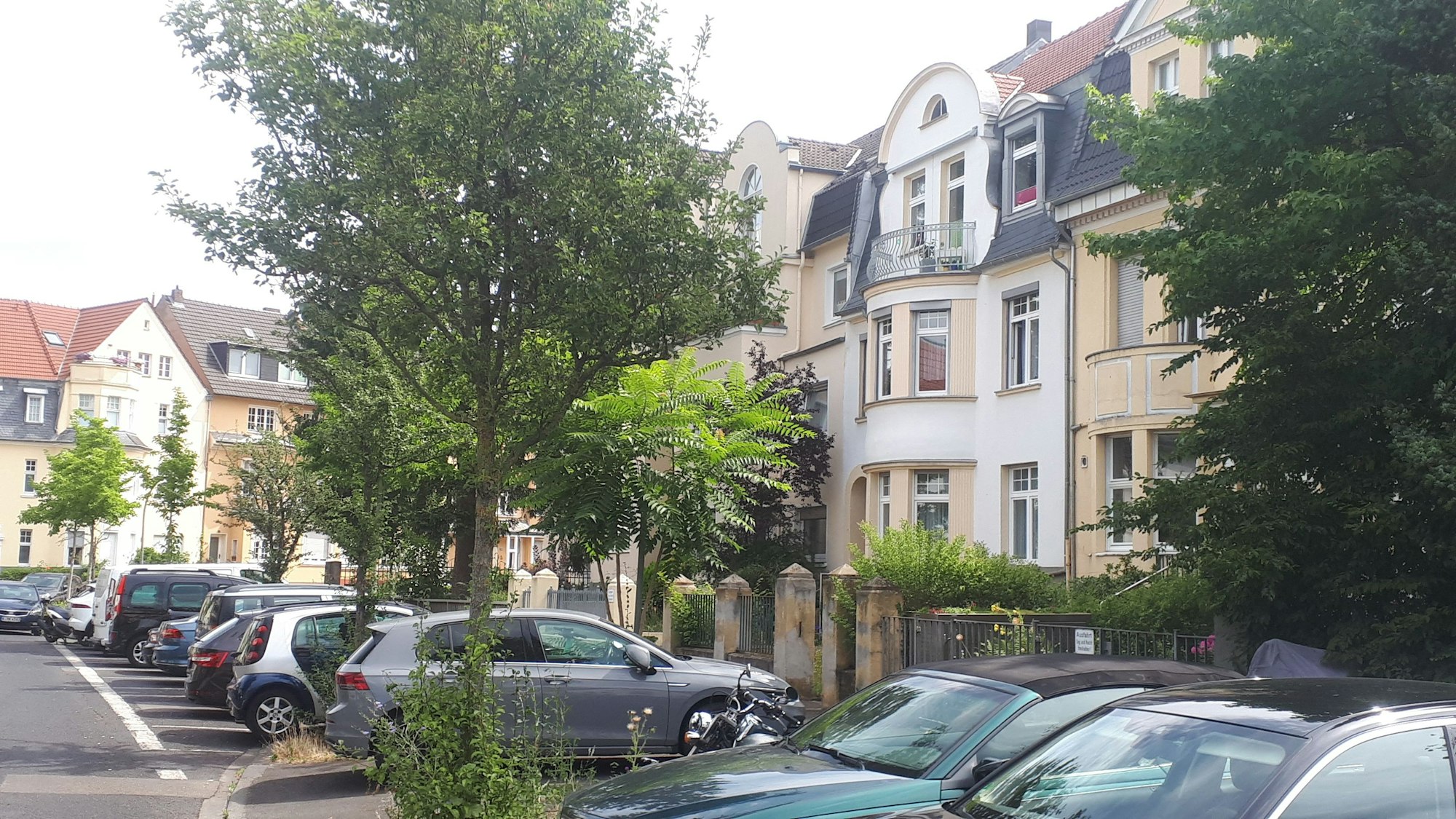 An einer Straße stehen Altbauvillen nebeneinander, davor parken Autos.