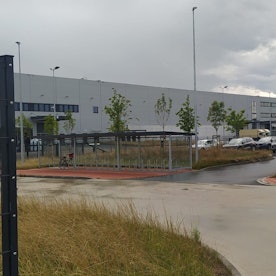 Junge Bäume stehen vor einem neuen, ganz in grau gehaltenen Industriegebäude.