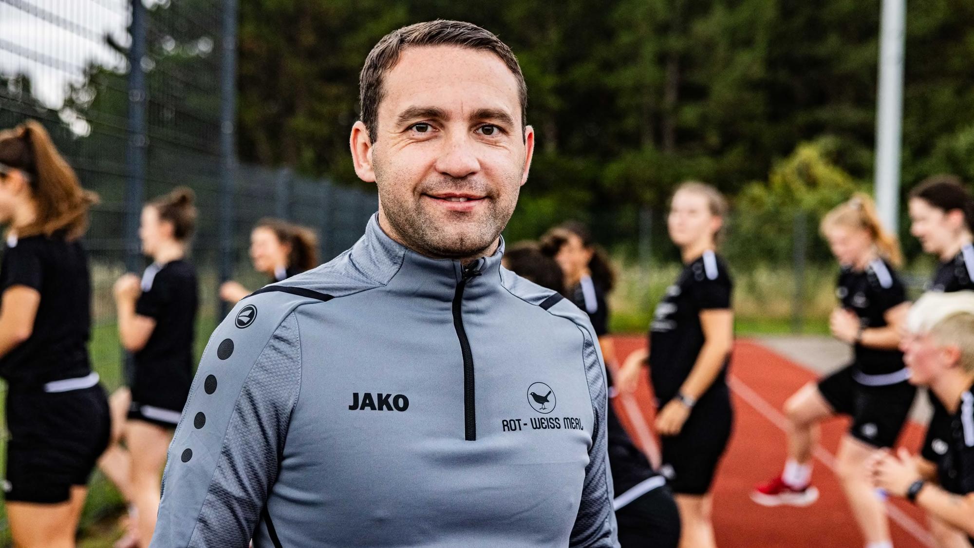 Der Trainer beim SV Rot-Weiß Merl, Rafael Tomaszko, im Vordergrund, im Hintergrund trainiert die Mannschaft.