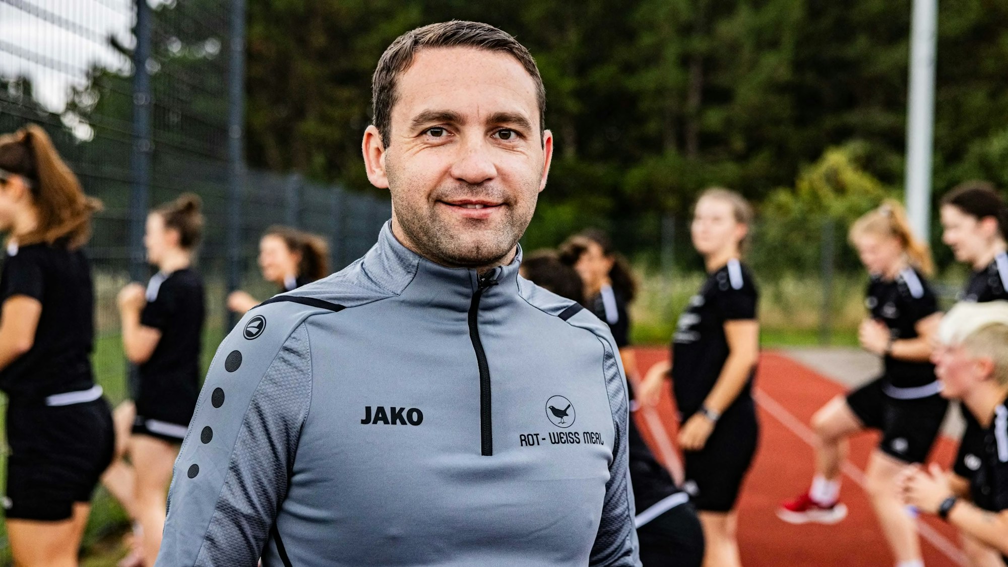 Der Trainer beim SV Rot-Weiß Merl, Rafael Tomaszko, im Vordergrund, im Hintergrund trainiert die Mannschaft.