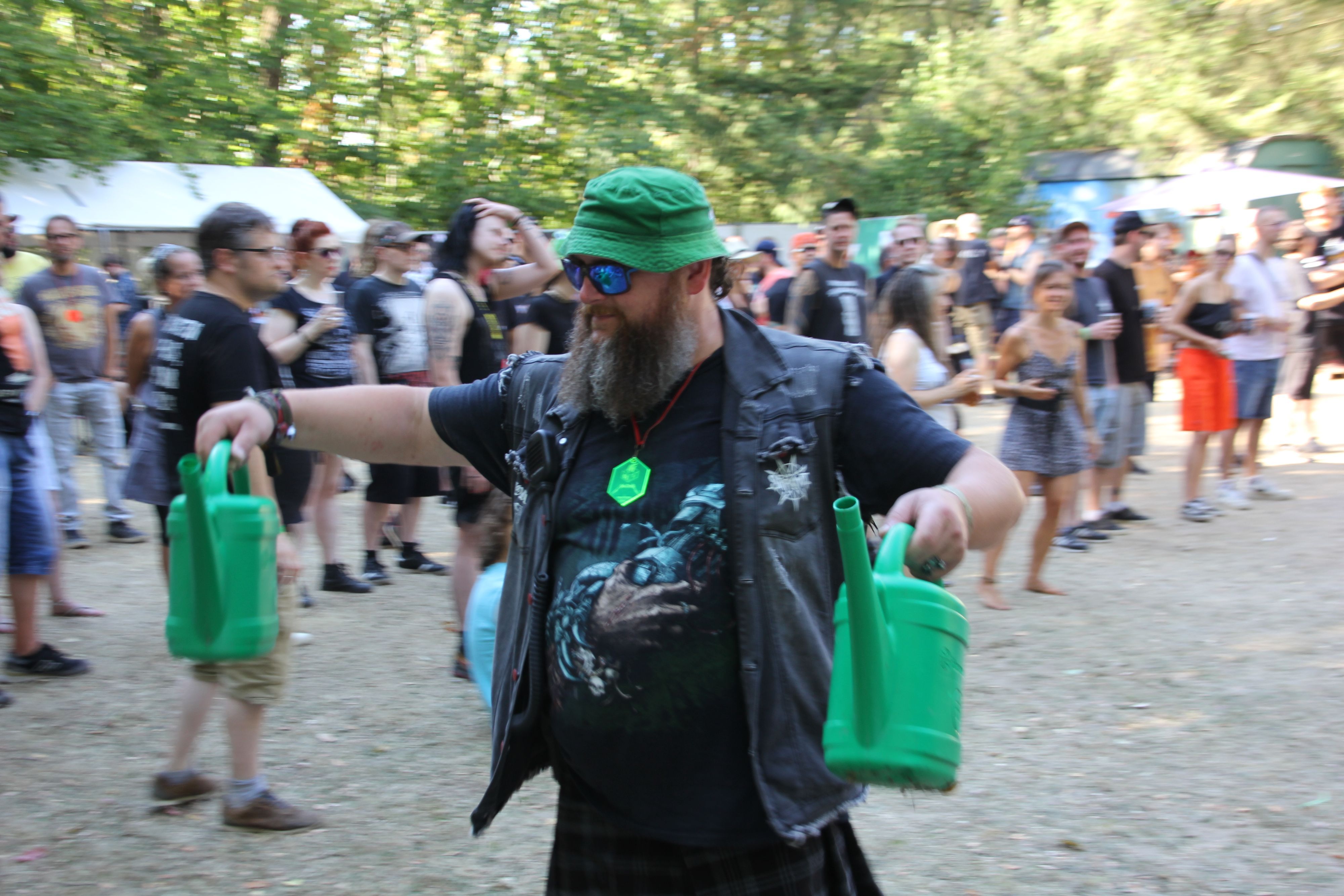 Ein Metal-Fan mit grünem Hut trägt zwei grüne Gießkannen durch das Publikum.