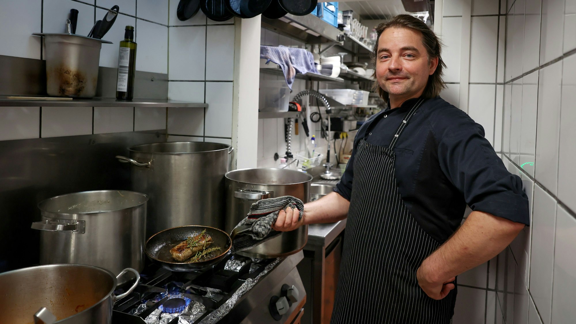 David Safanda vom Crevette Rosé steht in der Küche und brät ein Stück Fleisch in der Pfanne.