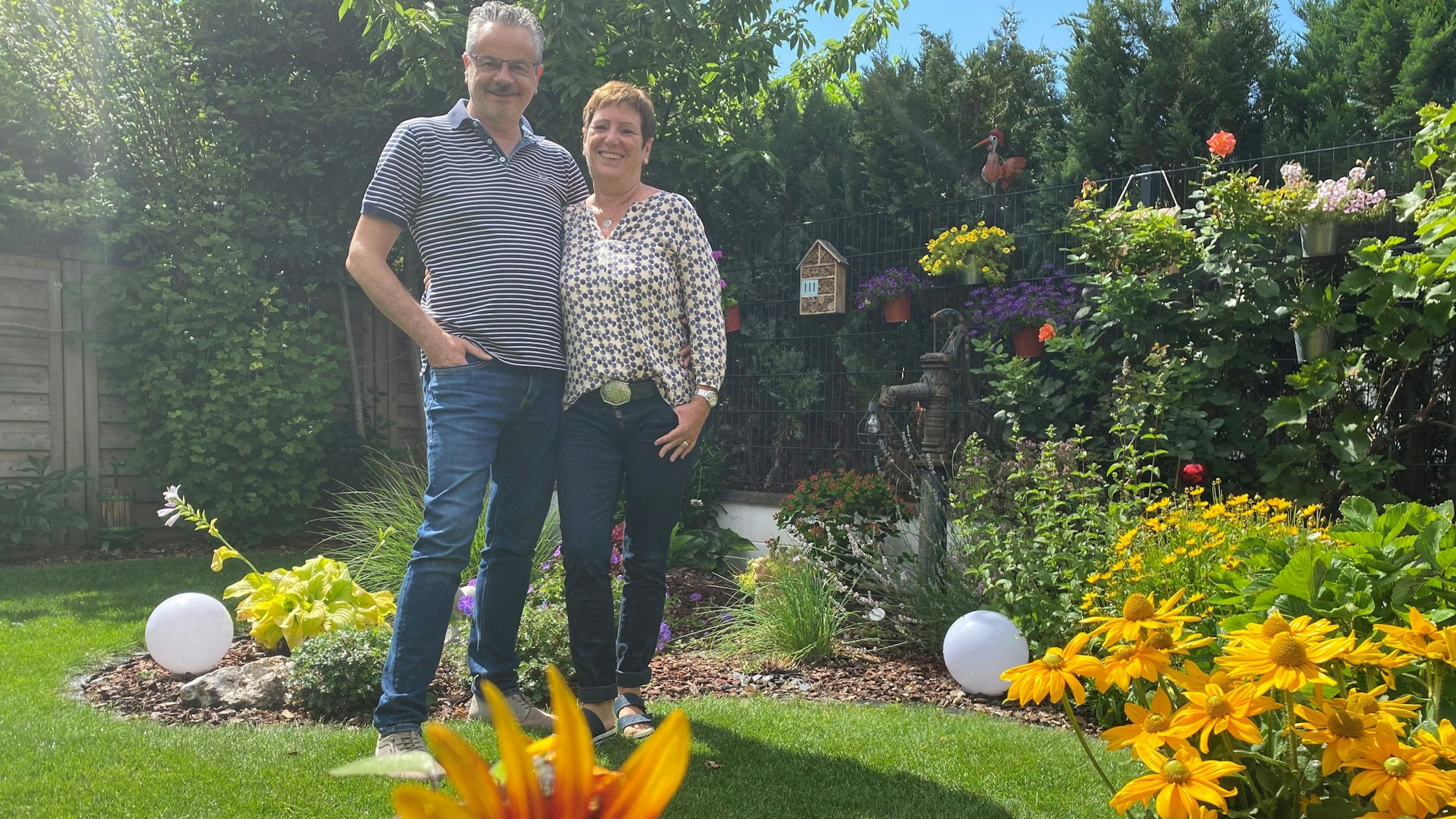Addi Kirfel und Marion Selbst stehen inmitten ihres gut bewässerten und blühenden Gartens.
