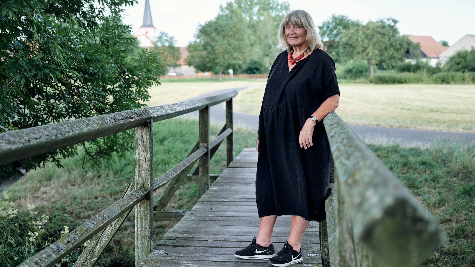 Alice Schwarzer steht auf einer alten Holzbrücke.