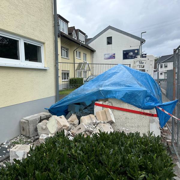 Ein Haufen Schutt liegt vor einem Haus. Er ist mit einer blauen Plane bedeckt.