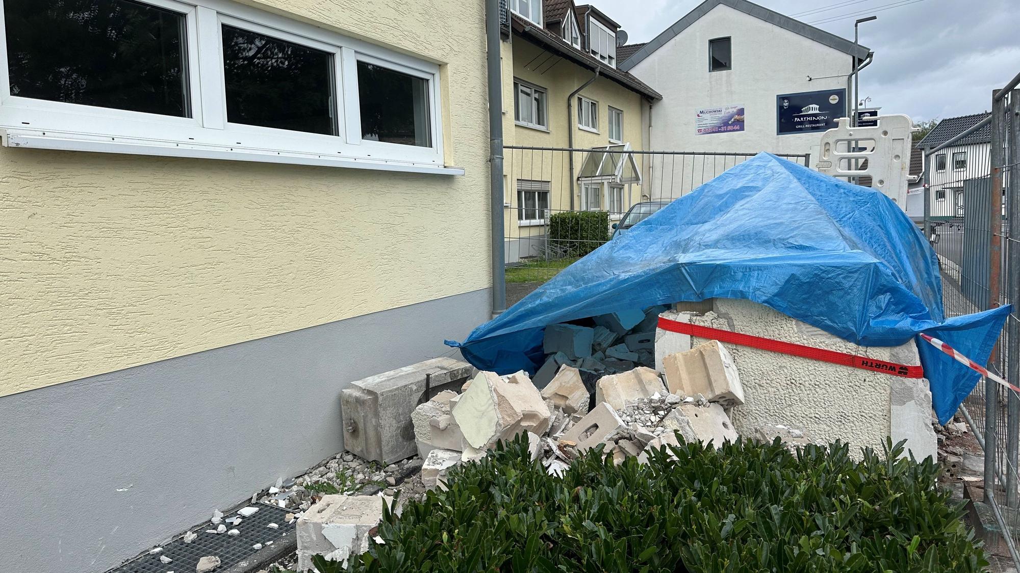 Ein Haufen Schutt liegt vor einem Haus. Er ist mit einer blauen Plane bedeckt.