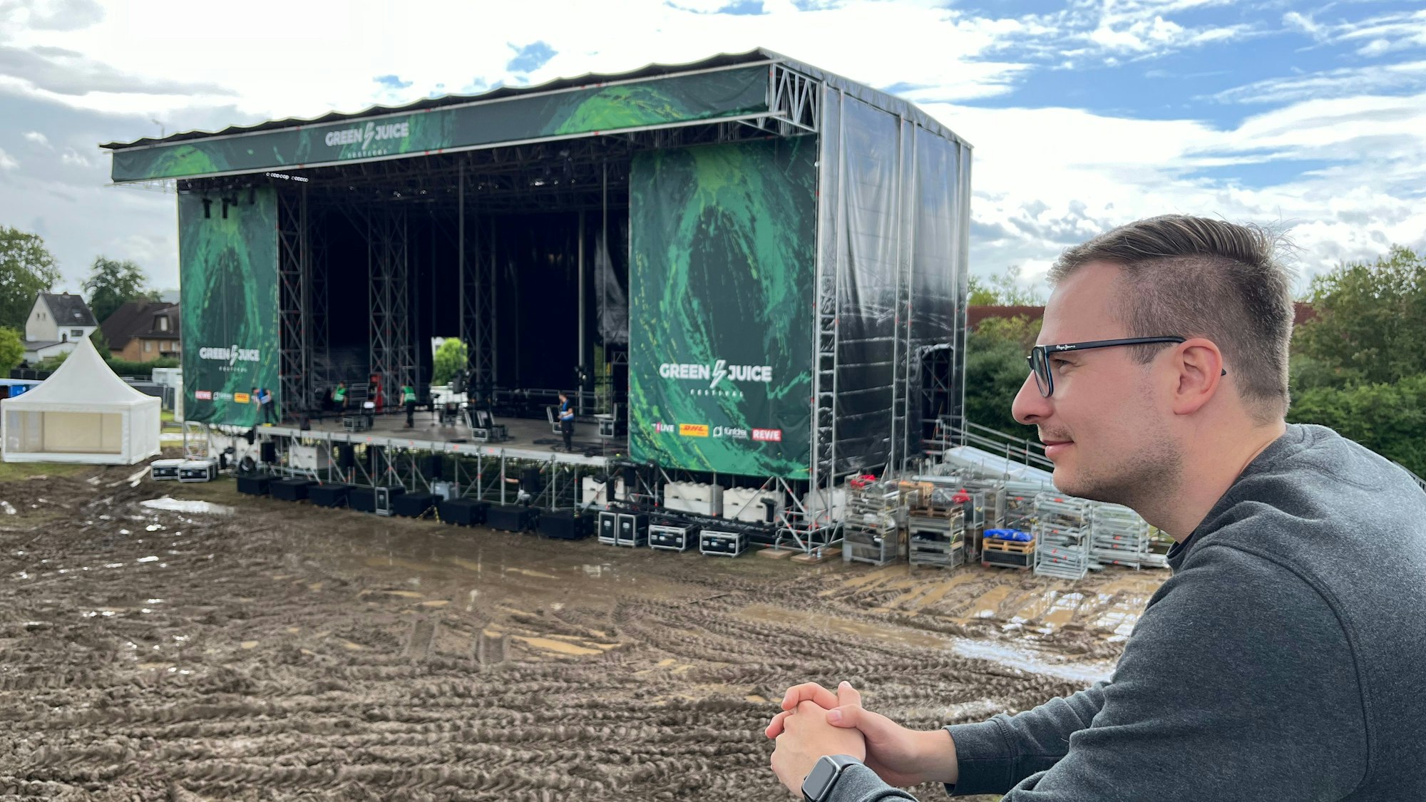 Ein junger Mann mit Brille steht vor einer Festivalbühne.