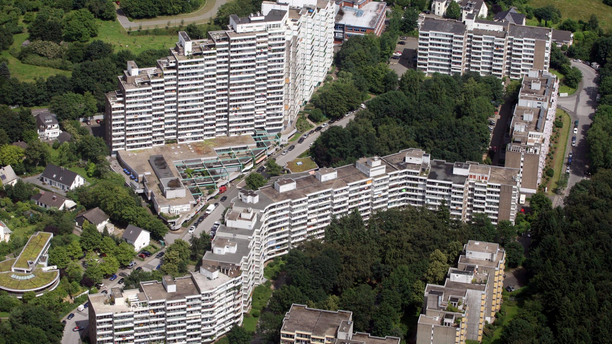 Zu sehen sind die Hochhausbauten, Block an Block aneinandergereiht, eingebettet in Grünfläche mit Bäumen.