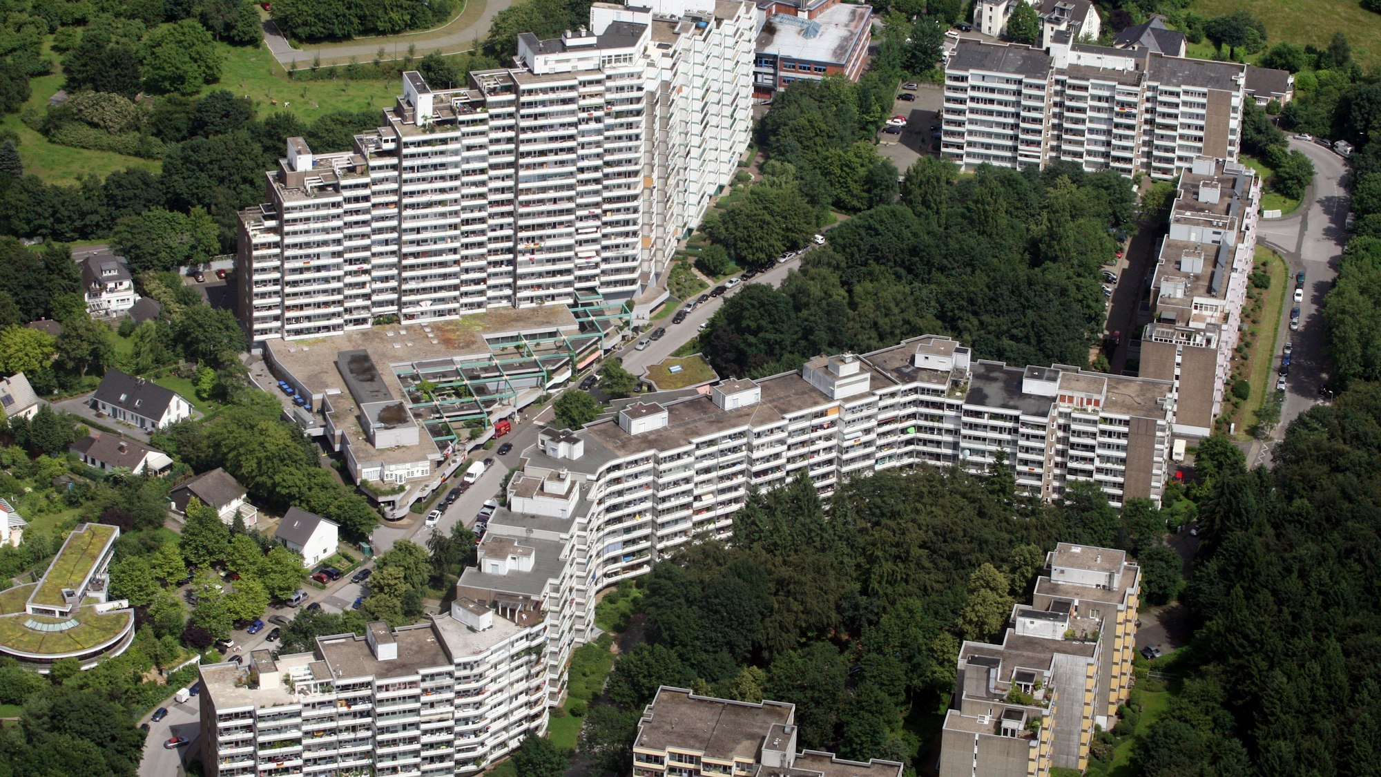 Zu sehen sind die Hochhausbauten, Block an Block aneinandergereiht, eingebettet in Grünfläche mit Bäumen.