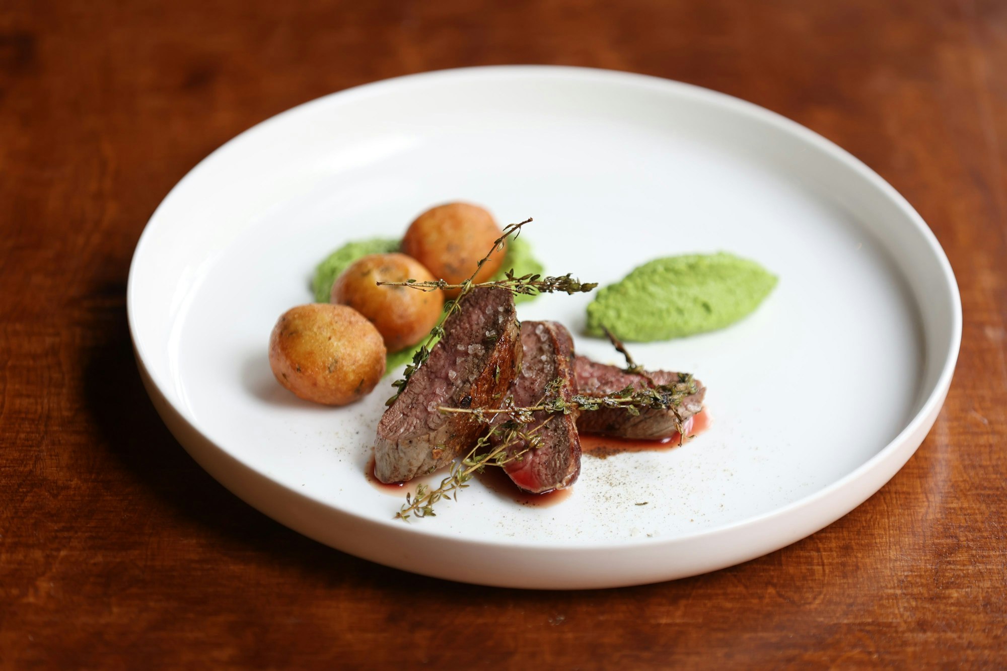 Lammrücken mit Zitronenthymian, Erbsenhumus und Ziegenkäse-Gougères liegen auf einem Teller