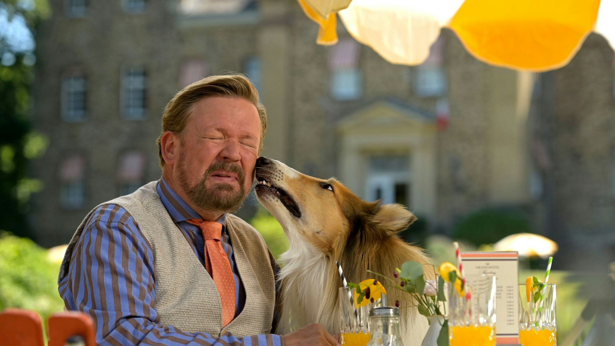Auf dem Bild ist Schauspieler Justus von Dohnany zu sehen, der von Lassie an die linke Wange gestupst wird.