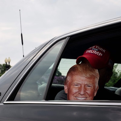 Ein Trump-Unterstützer hält einen Ausschnitt des Republikaners vor sein Gesicht. Trump soll am Donnerstag vor Gericht erscheinen, es geht um seine Rolle beim Sturm auf das Kapitol, das auf dem Foto im Hintergrund sichtbar ist.