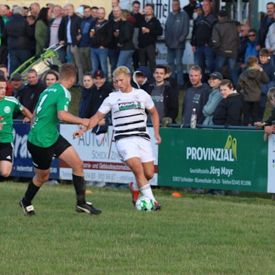 Ein Erftstädter Spieler kontrolliert, bedrängt von zwei Spielern aus Schöneseiffen, den Ball. Im Hintergrund sind die Zuschauer zu sehen.