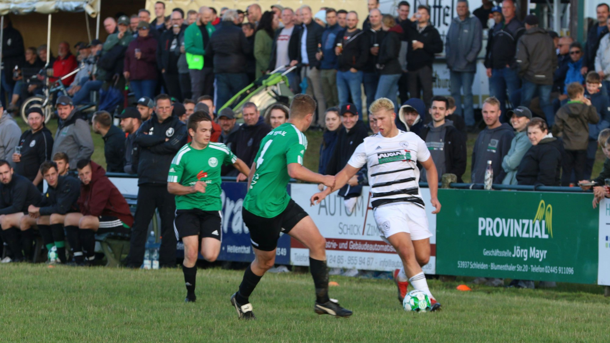 Ein Erftstädter Spieler kontrolliert, bedrängt von zwei Spielern aus Schöneseiffen, den Ball. Im Hintergrund sind die Zuschauer zu sehen.