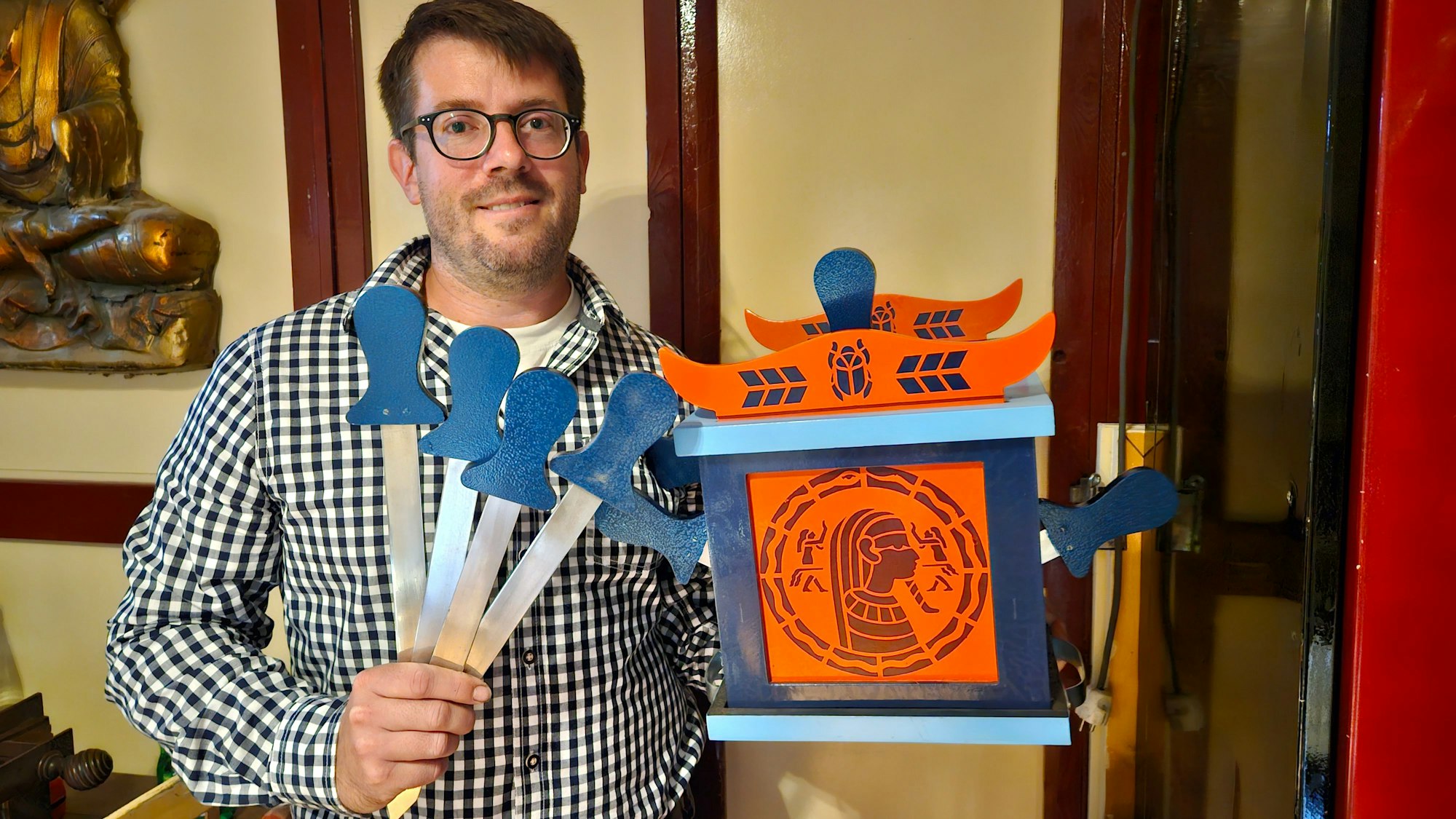 Ein Mann mit kariertem Hemd und Brille zeigt Schaudolche und einen bunten Kasten.