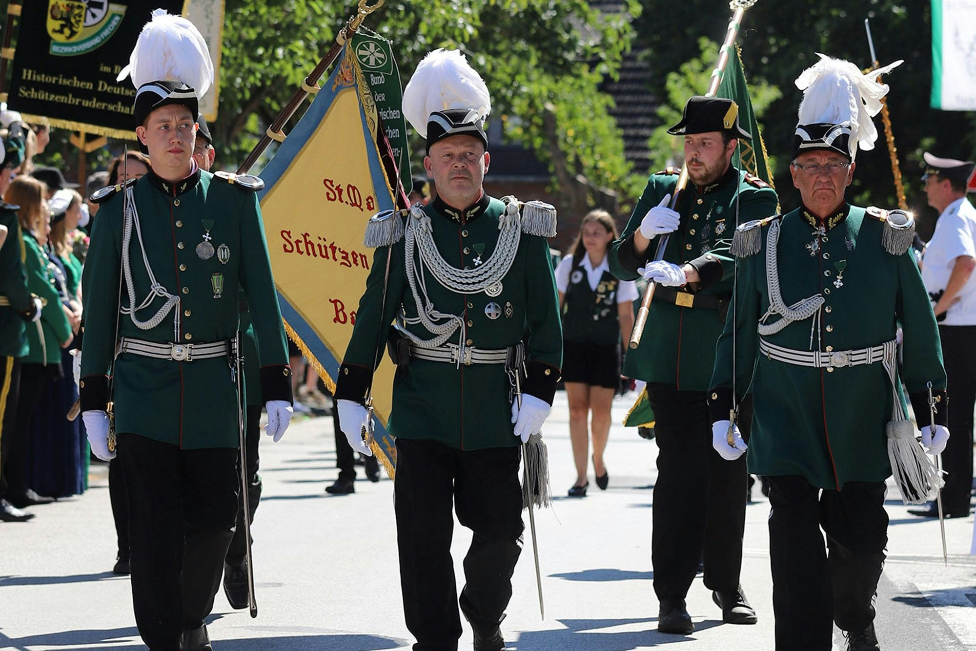 Männer in Schützenuniform mit Fahnen marschieren an Publikum vorbei.