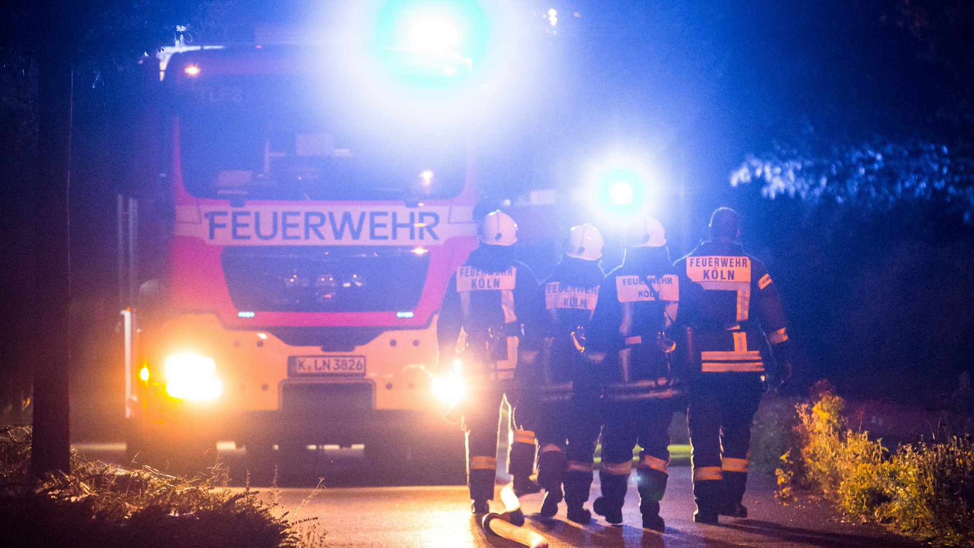 Vier Feuerwehleute laufen im Dunkeln vor ihrem Einsatzwagen entlang.