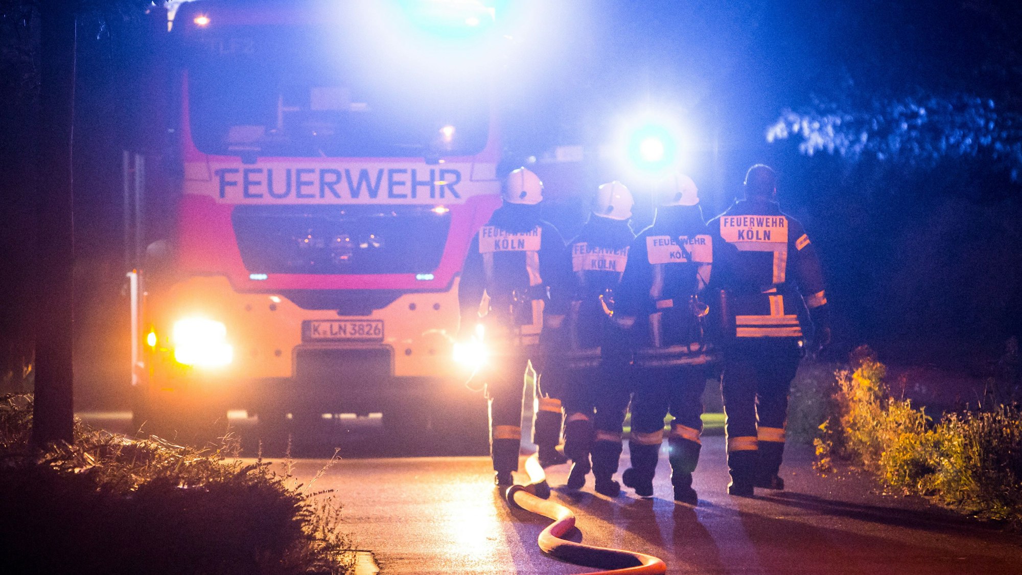 Vier Feuerwehrmänner gehen bei einem Einsatz in der Nacht zu ihrem Fahrzeug.