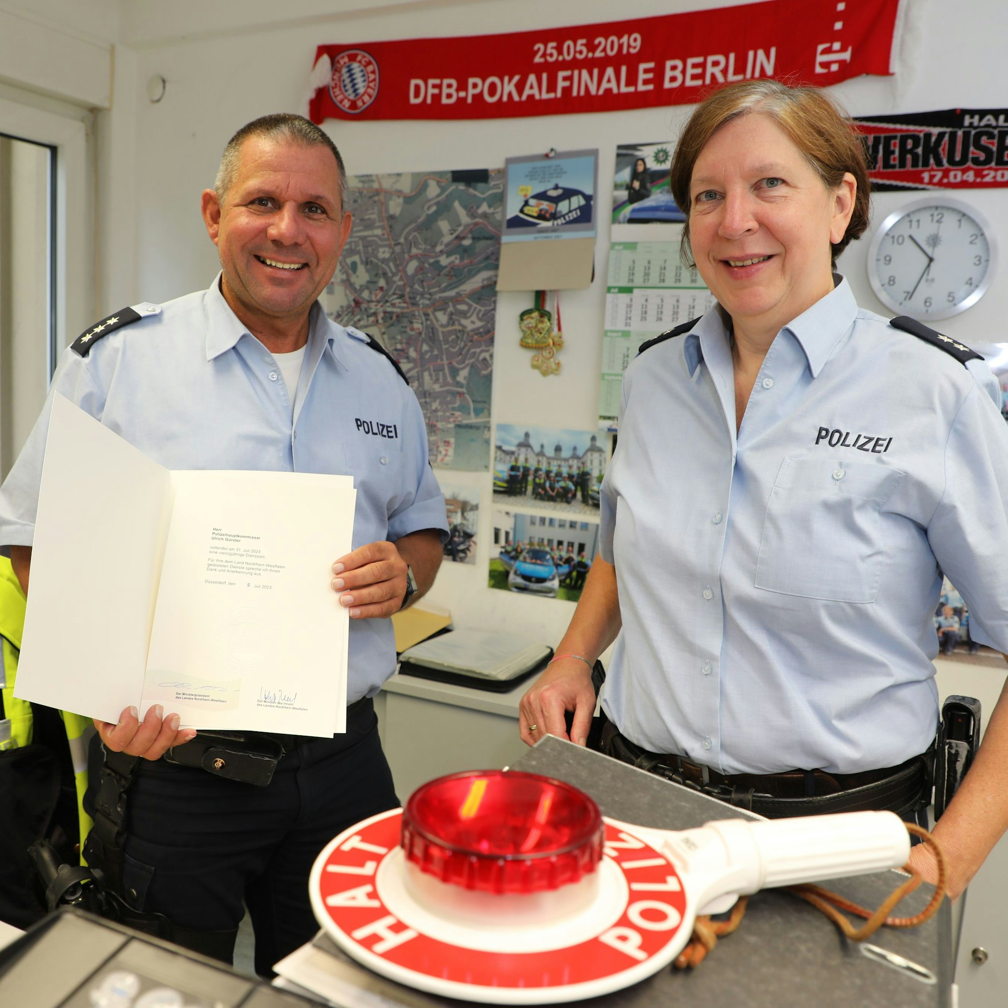 Bezirksdienstbeamter Ulrich Gürster hält die Urkunde zu seinem 40-jährigen Dienstjubiläum in den Händen. Neben ihm steht seine neue Kollegin, Alexandra Schneiders.