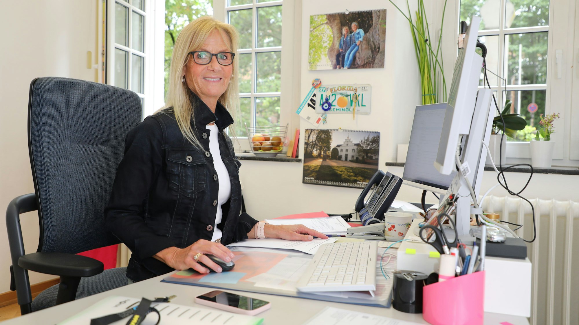 Eine Frau sitzt mit Brille an einem Schreibtisch.