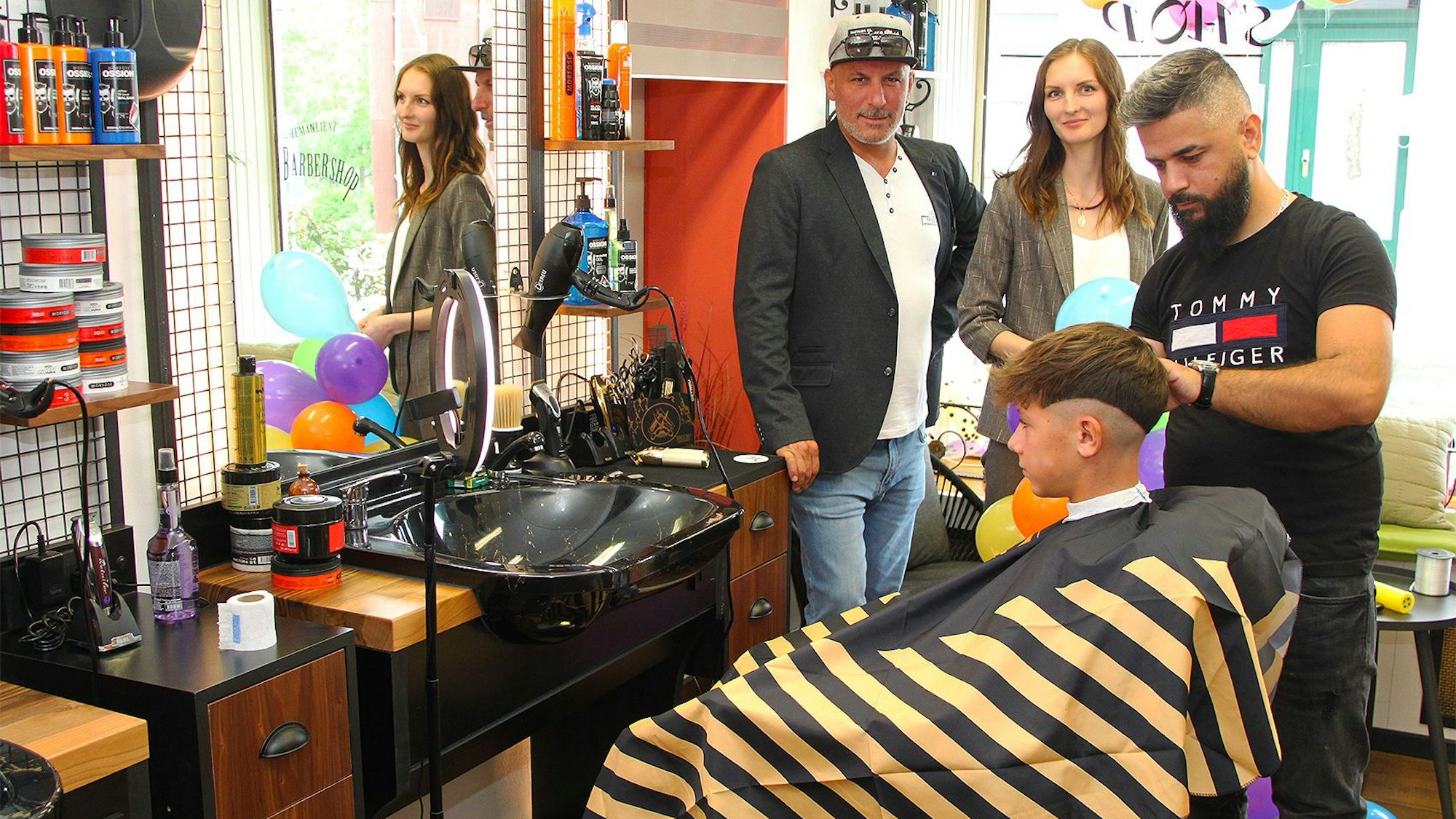 Im Barber-Shop schneidet Friseurmeister Mohammed „Jan“ Golak Ben aus Blankenheim die Haare. Im Hintergrund stehen Geschäftsinhaber Cetin Erdogan und Vira Lavriv, die die Postfiliale nebenan führt