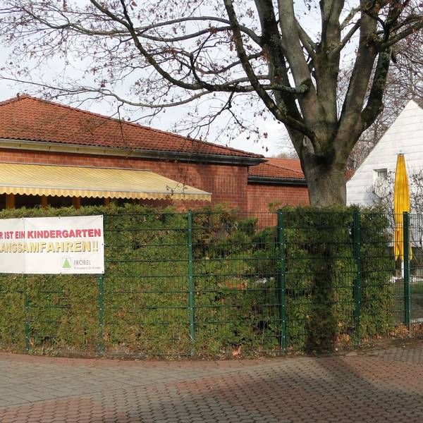 Das Gebäude ragt hinter einer Hecke hervor.