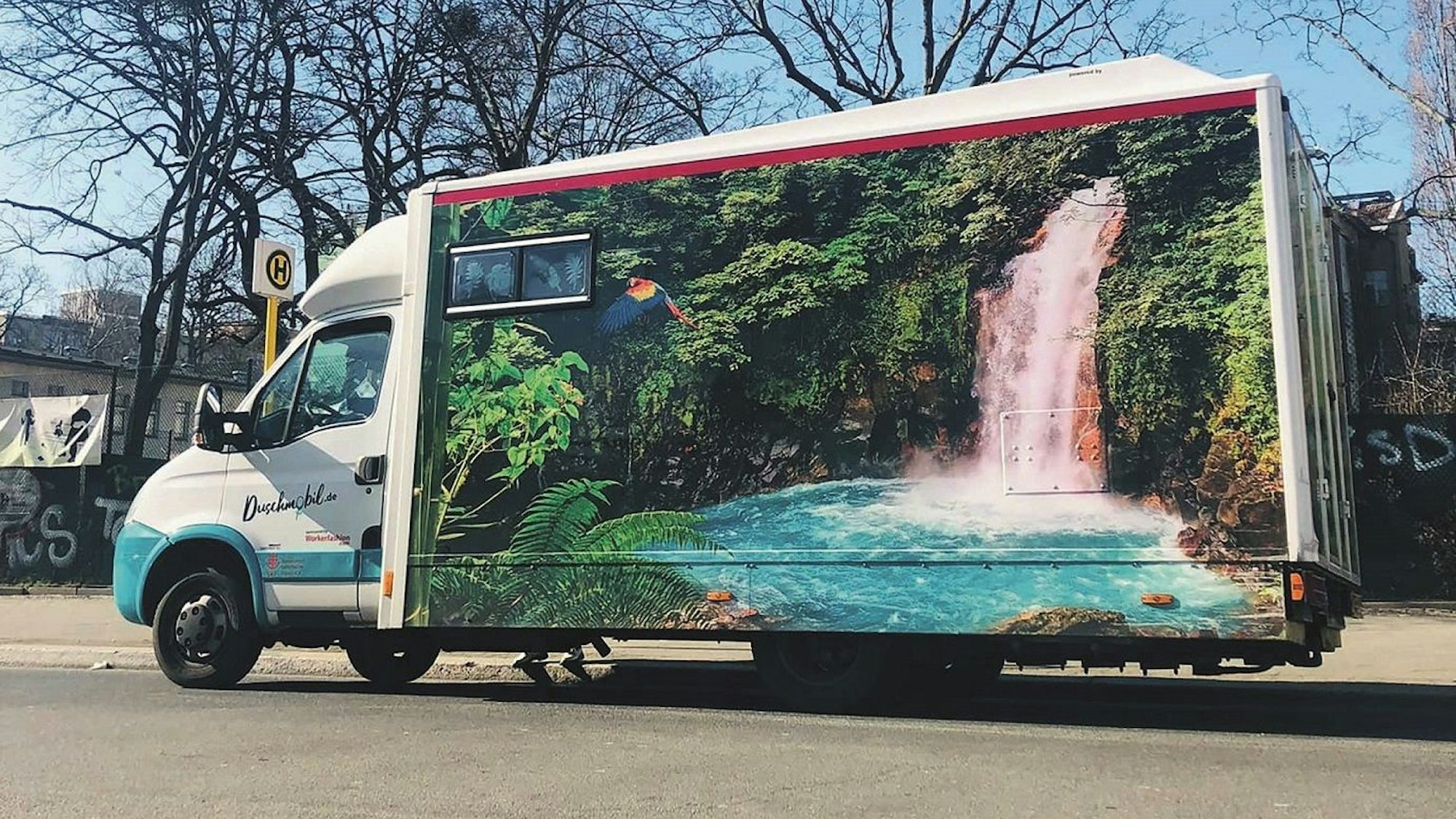 Ein großer Transporter mit einem aufgemalten Wasserfall steht auf einer Straße.