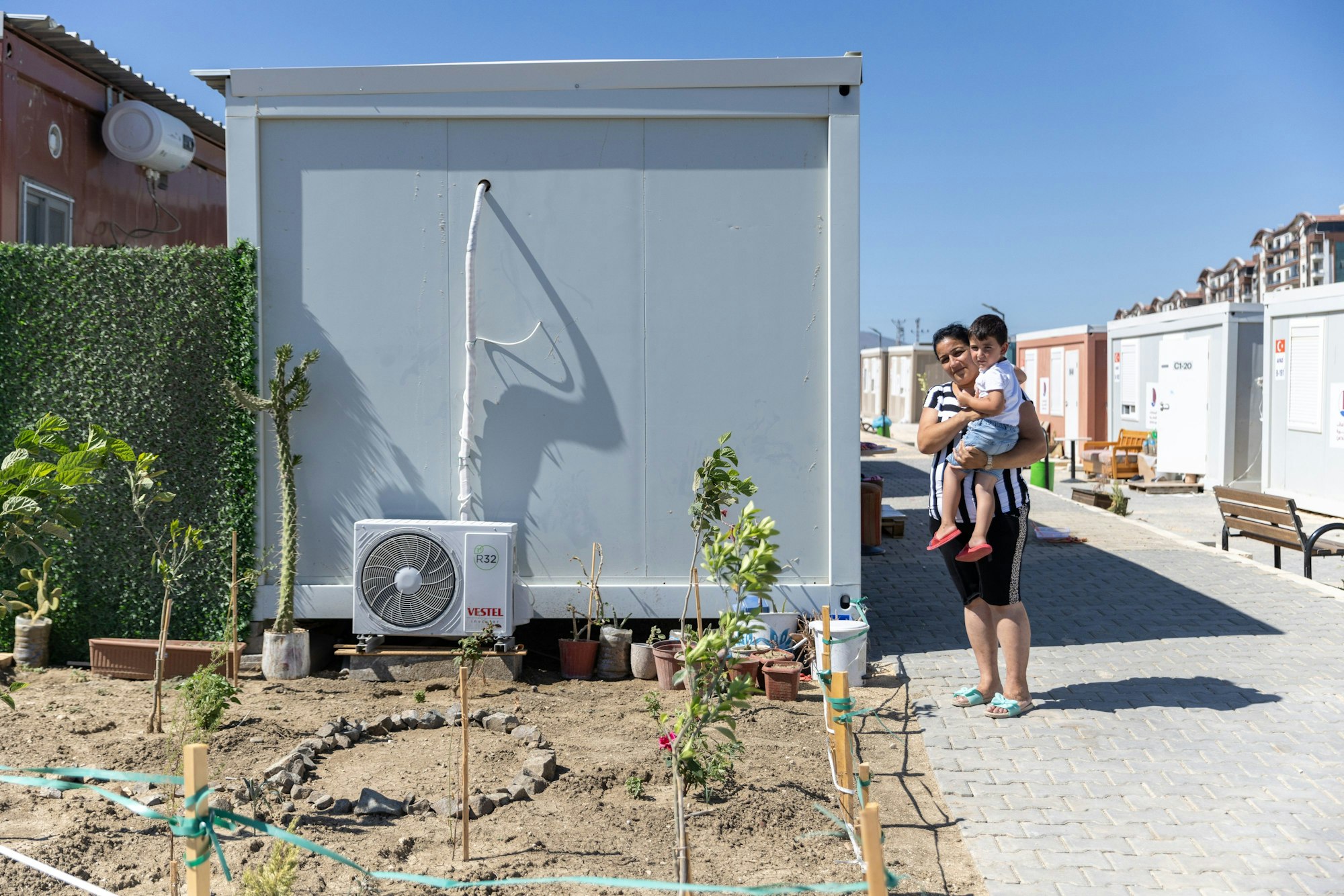 Derman Demirkol (37) und ihr Sohn stehen vor einem Schiffscontainer im ‚Katar-Containerlager‘, in dem sie derzeit leben. Ihr Haus wurde bei dem Erdbeben vor fast sechs Monaten zerstört.