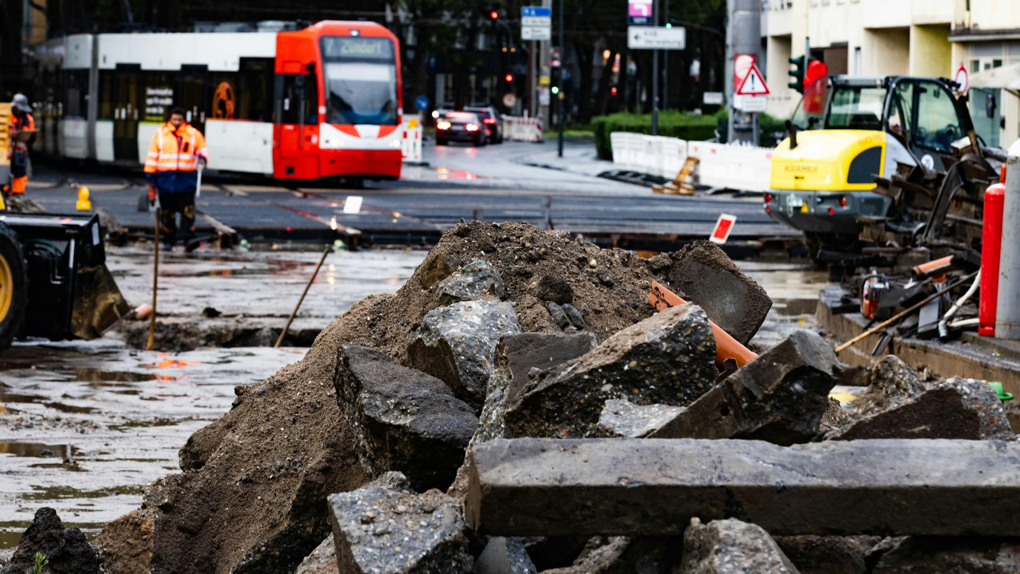 Eine aufgerissene Straße, auf der Schutt liegt. Eine KVB Bahn im Hintergrund.