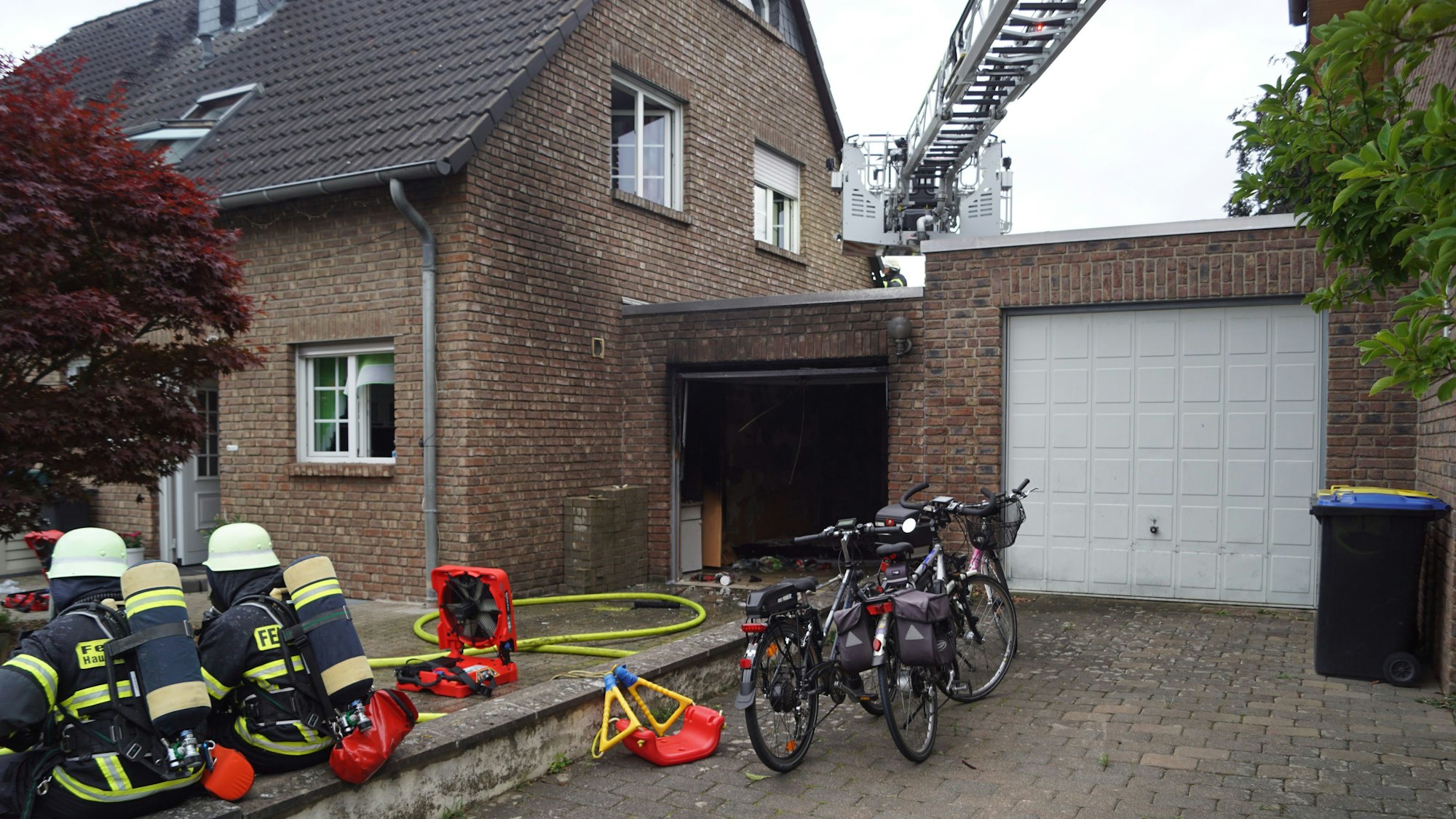 Das Bild zeigt die ausgebrannte Garage. Auf einer Mauer sitzen zwei Feuerwehrleute.