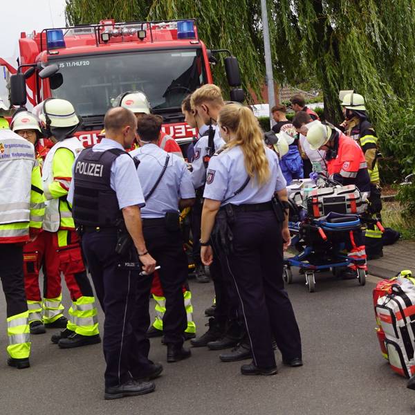 Das Bild zeigt mehrere Beamte und Einsatzkräfte. Rechts im Bild wird ein Mann behandelt.