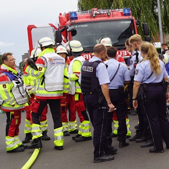 Das Bild zeigt mehrere Beamte und Einsatzkräfte. Rechts im Bild wird ein Mann behandelt.